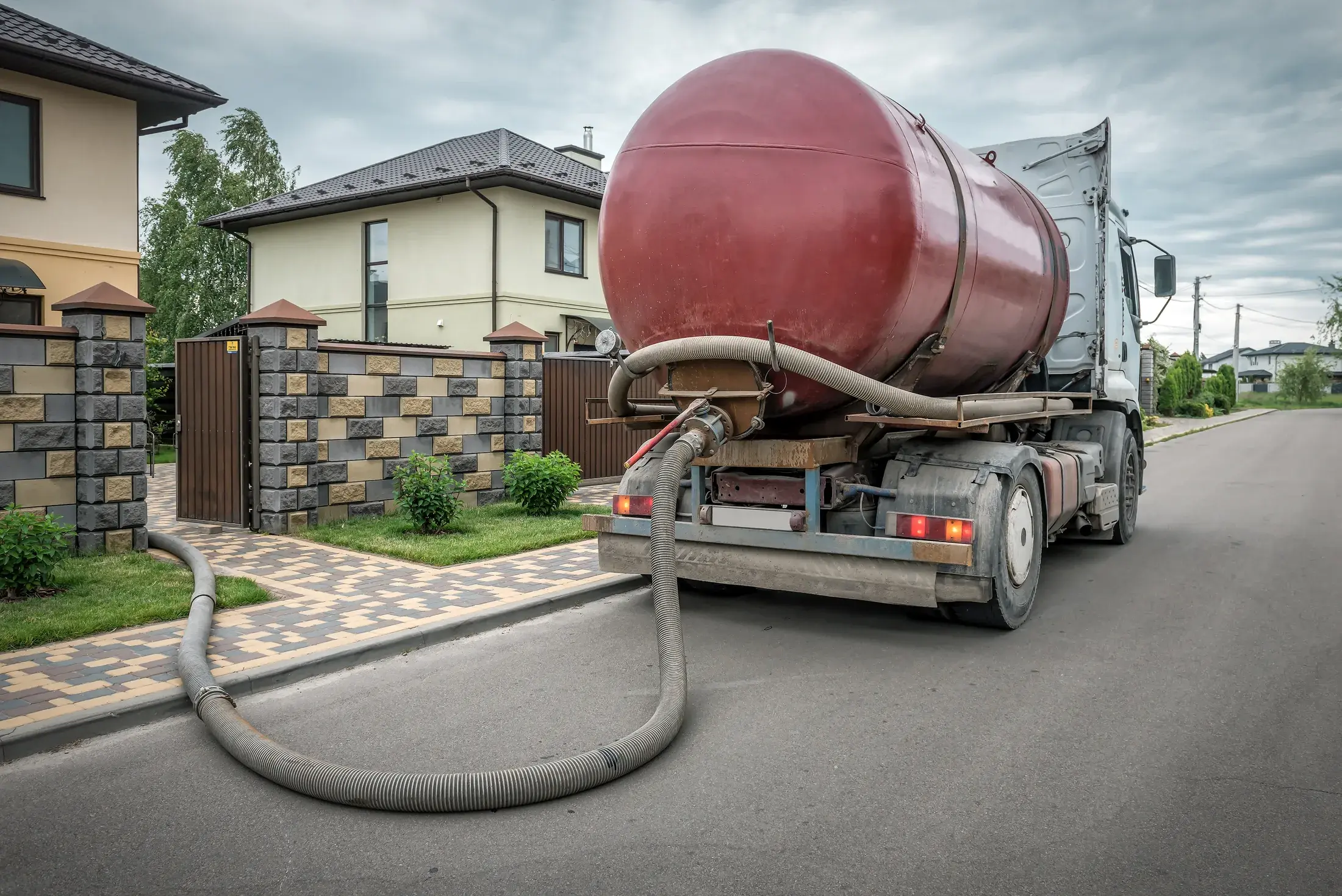 Septic pumping truck with its vacuum hose extended along a residential driveway during a pump-out service call
